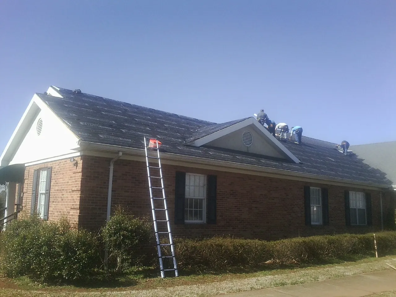 Crew tearing shingles off a brick ranch roof with a ladder set — Emergency Roof Repair work by our crew in Crest Hill