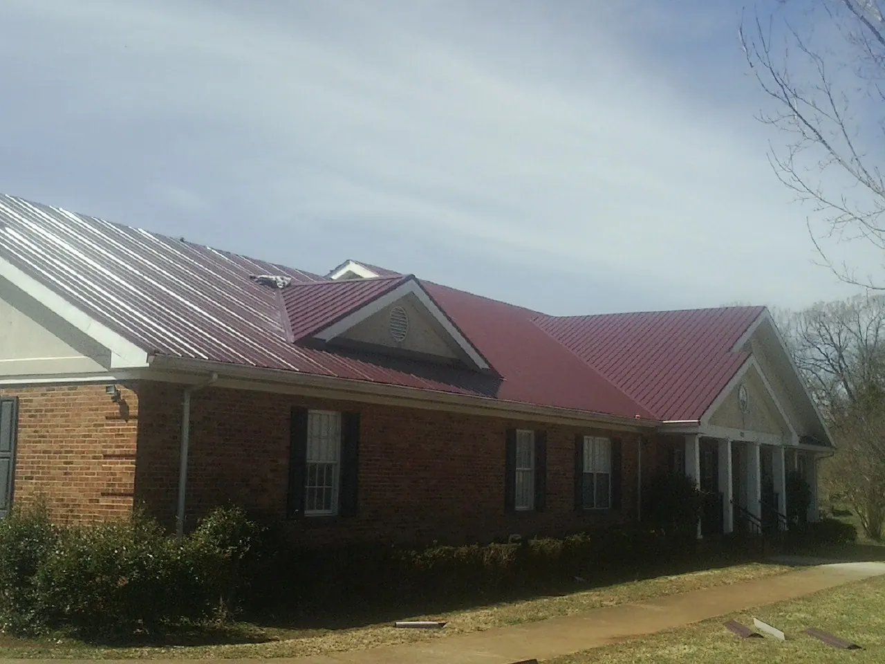 Red metal roof with gabled entries on a long brick building, from a Hail Damage Roof Repair job in Crest Hill