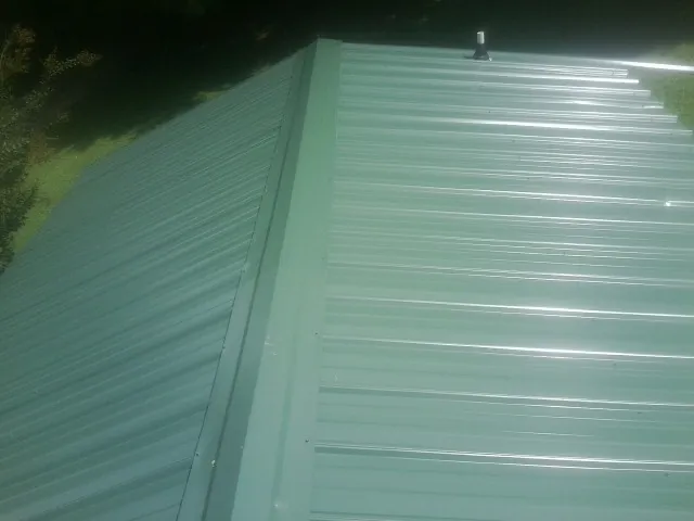 New green metal panels meeting at the ridge of a roof — Flat Roof Repair work by our crew in Crest Hill