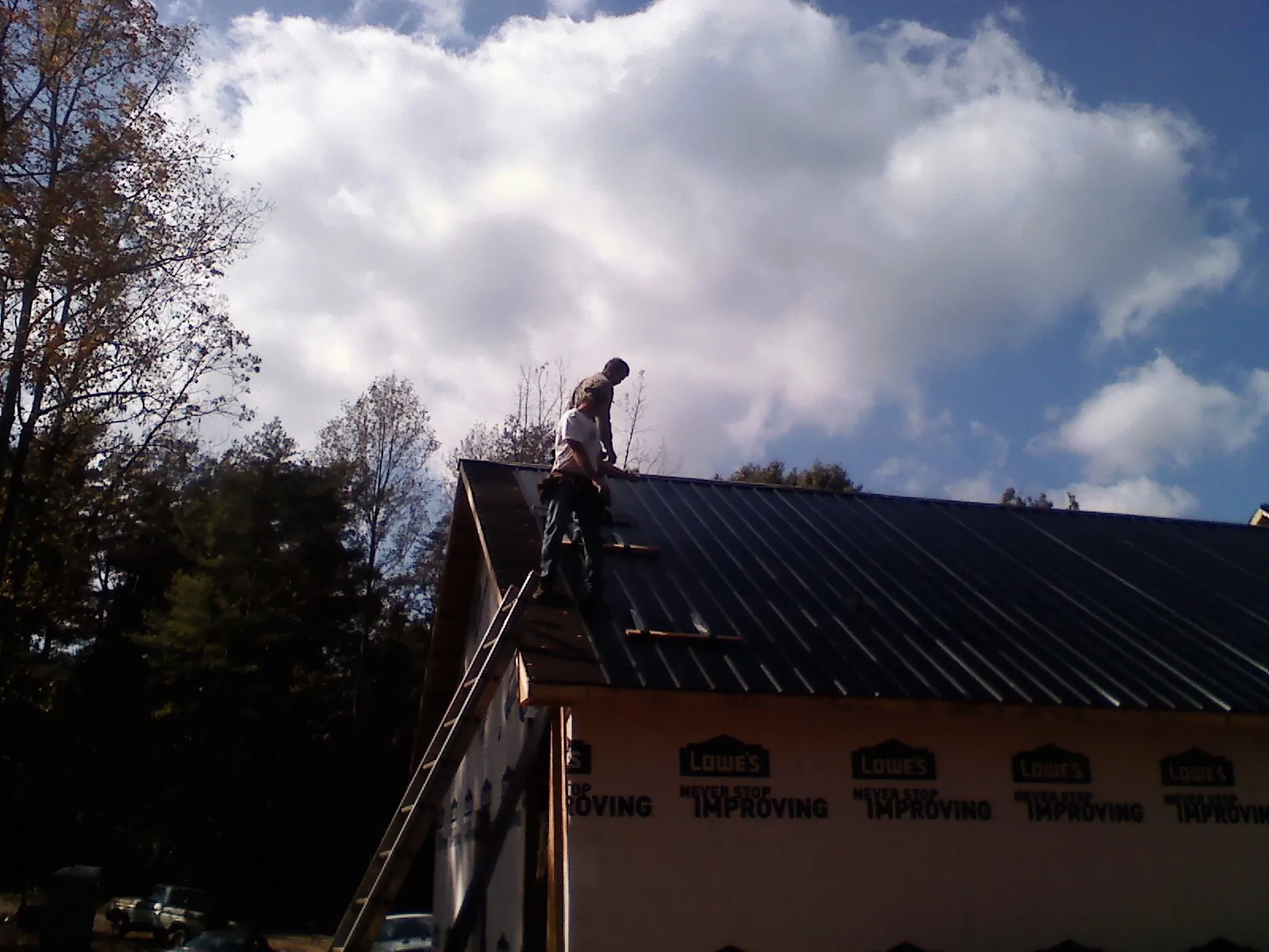 Roofer fastening dark metal panels high against a cloudy sky, from a Roof Inspection job in Crest Hill