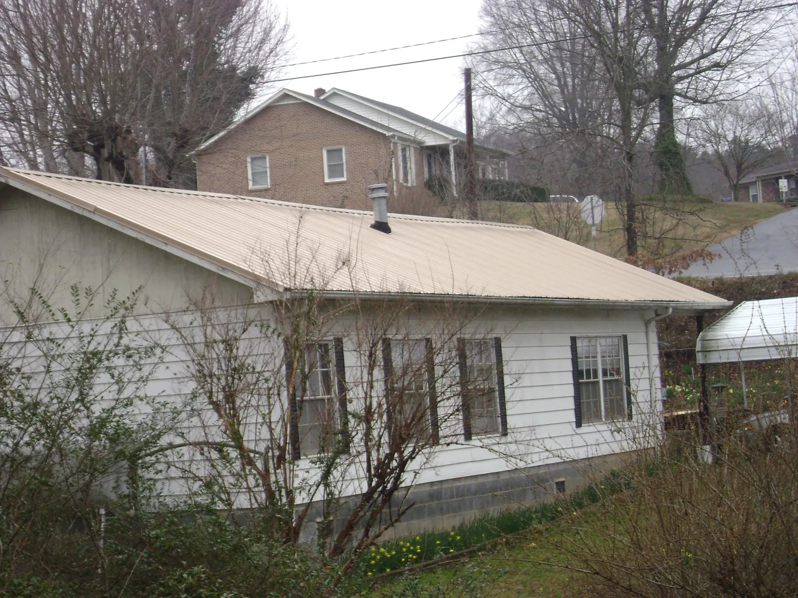 Tan metal roof on a white sided house set into a hillside — Commercial Roofing by Roofing Brothers in Crest Hill